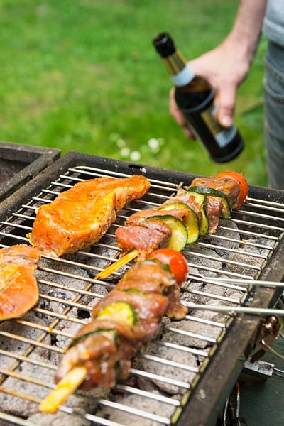 Man holding beer bottle at barbecue grill with meat
