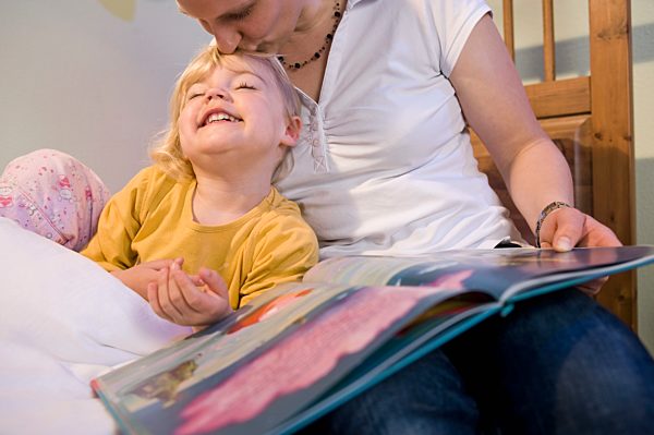 Mother kissing forehead of daughter and holding book