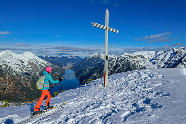 Woman back country skiing by summit cross at Baerenkopf near Achensee, Karwendel Mountains, Tyrol, Austria