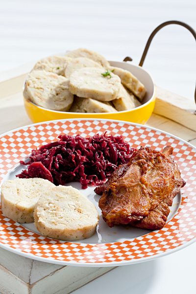 Plate of pork knucke with slices of bread dumpling and red cabbage in wooden tray, close up