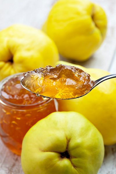 Four quinces (Cydonia oblonga), a spoon and a glass of quince marmalade on wooden table