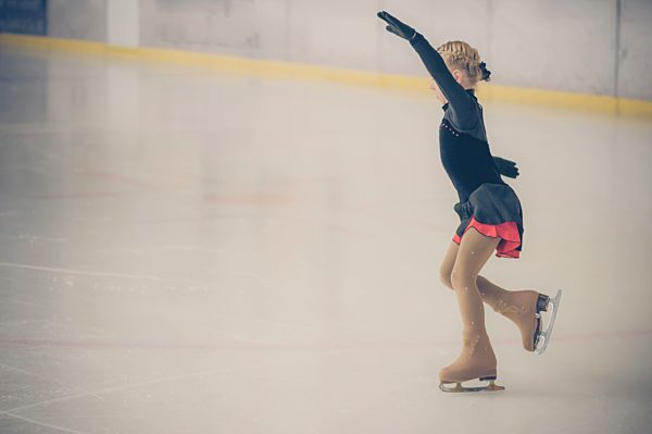 Young female figure skater moving on ice rink at competition