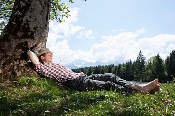 Germany, Bavaria, Mid adult man lying on grass under tree