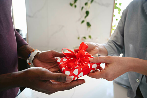 Couple exchanging romantic gift with red heart wrapping indoors