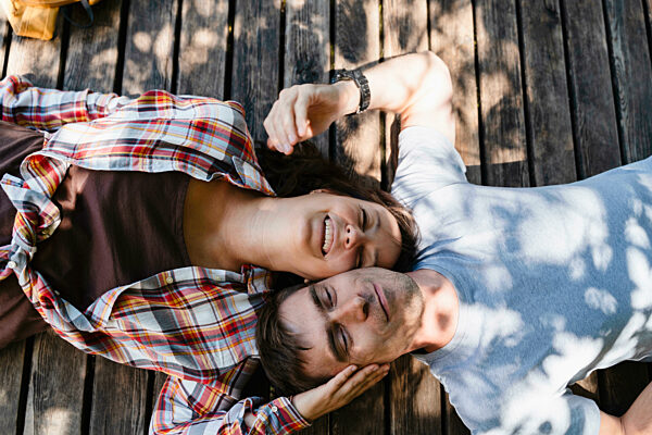 Laughing couple lying outdoors on wooden floor enjoying happiness