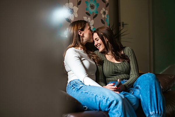 Happy couple sharing a kiss on sofa at home in casual clothing
