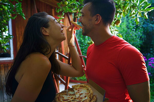 Couple feeding each other pizza outdoors in summer with joyful expressions
