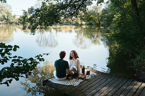 Couple relaxing by the pond enjoying a romantic picnic outdoors