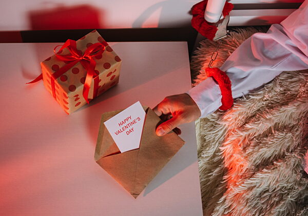 Hand with handcuff reaching for Valentine's Day card and gift on table