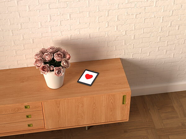 Tablet with heart symbol and vase of roses on wooden sideboard
