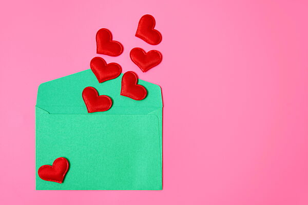 Green envelope with red hearts on pink background for Valentines Day