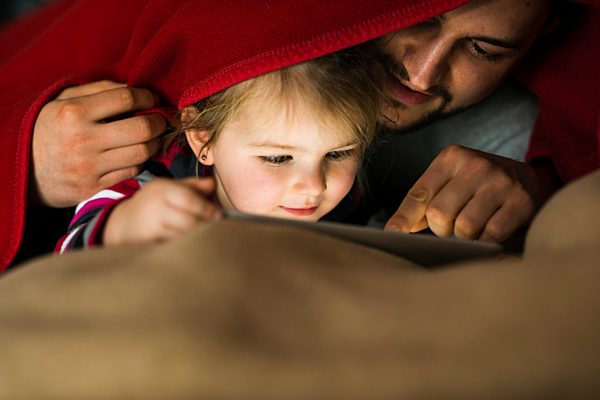 Father and daughter with digital tablet under blanket