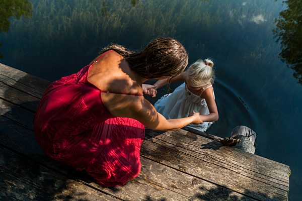 Mother on jetty holding daughter in summer dress in lake