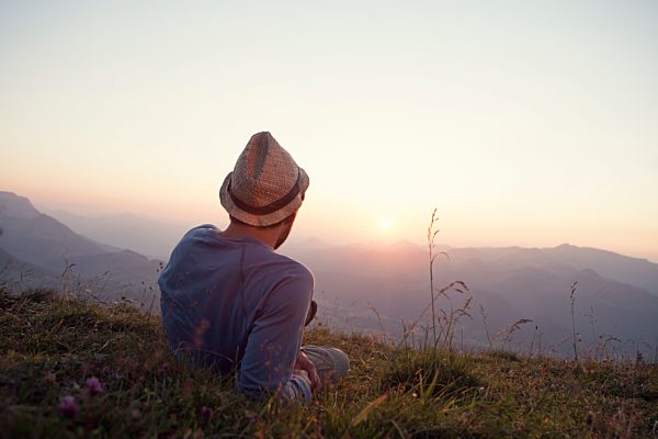 Austria, Tyrol, Unterberghorn, man resting on alpine meadow at sunset