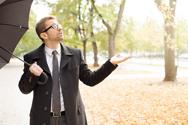 Businessman in a park with umbrella checking the weather