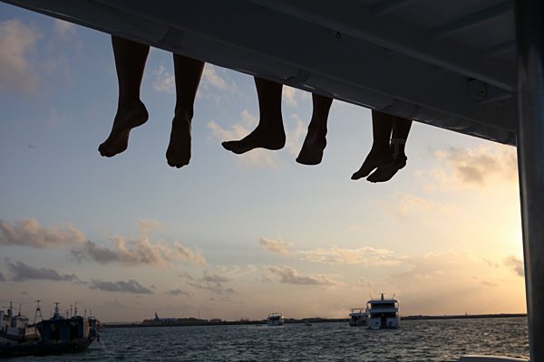 Maledives, South Male Atoll, legs of three people sitting on a jetty at evening twilight