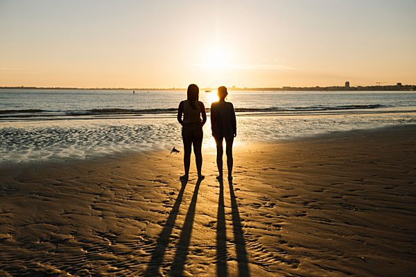 France, Pornichet, silhouettes of two women standing on the beach at sunset
