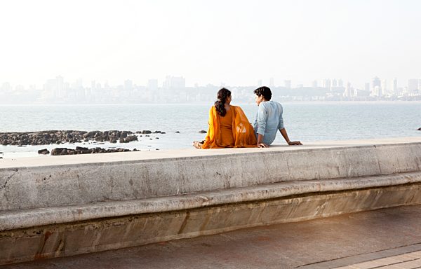India, Mumbai, Young couple sitting at beach promenade, looking at ocean