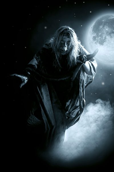 Witch riding on broom in front of full moon and starry sky