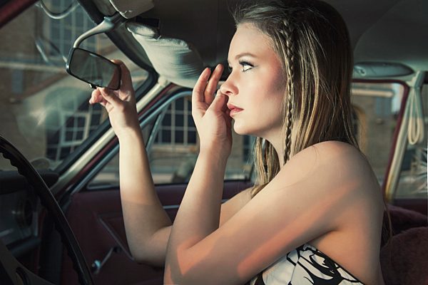 Young woman checking her make up in rear-view mirror of vintage car