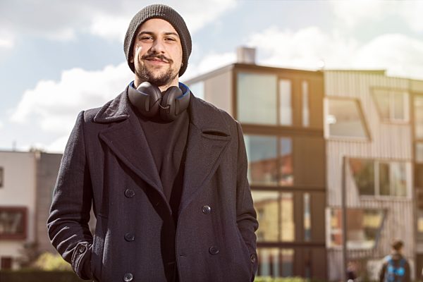 Portrait of smiling young man with headphones wearing wool cap and black clothes