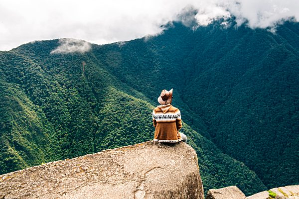 Peru, Machu Picchu region, man sitting on rock spur, looking at view