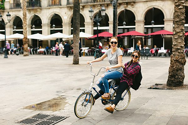 Spain, Barcelona, two happy young women sharing bicycle in the city