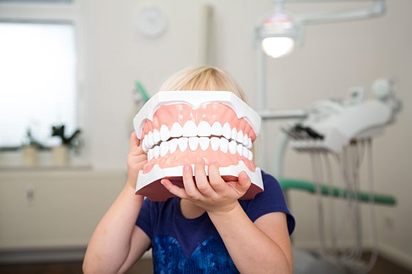 Girl in dental sugery holding big tooth model