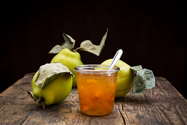 Quinces and a glass of quince jam  on wood