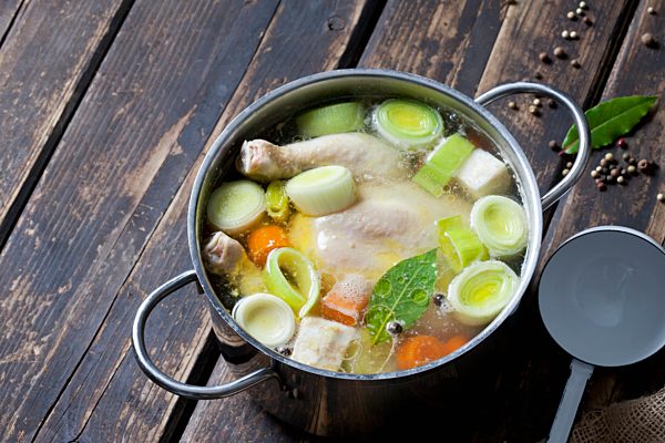 Cooking pot with raw corn-fed chicken, onion, herbs and greens