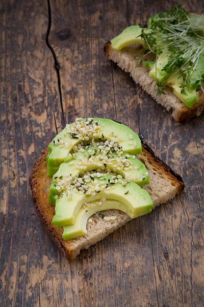 Slice of toasted bread with acocado, cress and hemp seeds on wood