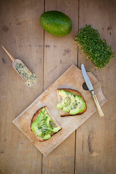 Slice of toasted bread with acocado, cress and hemp seeds on wooden board