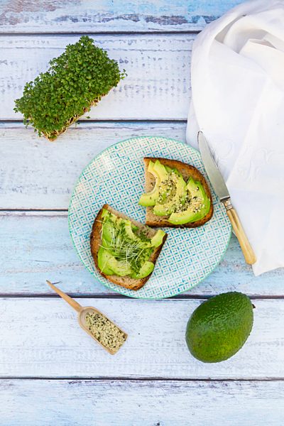 Slice of toasted bread with acocado, cress and hemp seeds on a plate