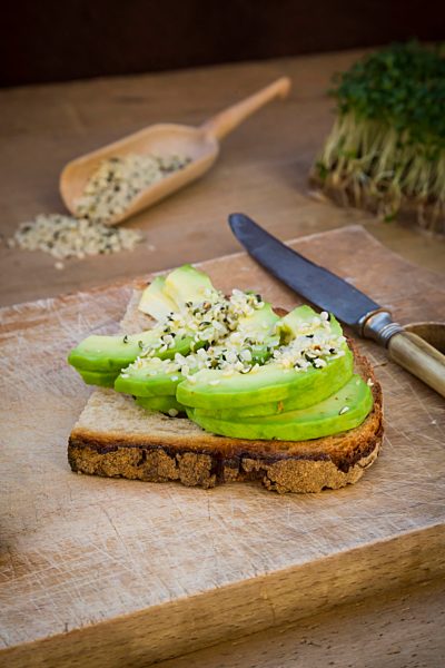 Half slice of toasted bread with acocado and hemp seeds on wooden board