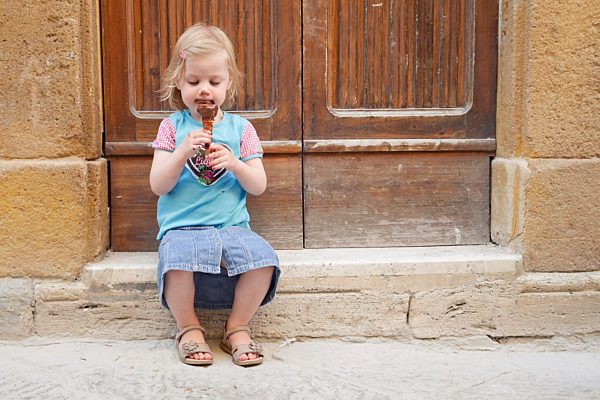 Girl with chocolate ice cream cone sitting on stoop
