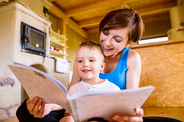 Pregnant mother looking at picture book with her little son