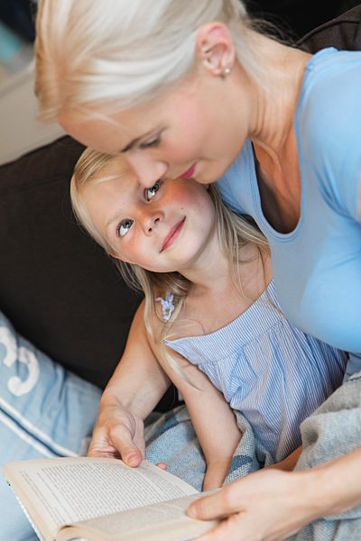 Mother and little daughter sitting together on couch with a book