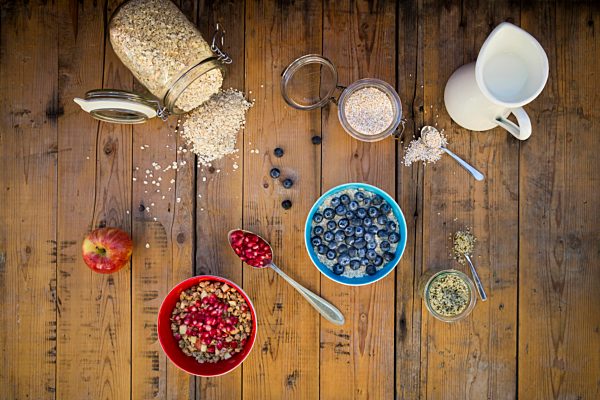 Bowl of overnight oats with blueberries and bowl of granola with pomegranate seed and red apple on wood