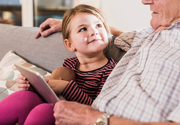 Grandfather reading out story for his granddaughter, using ebook
