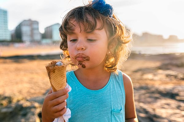 Portrait of little girl eating chocolate icecream on the beach at sunset