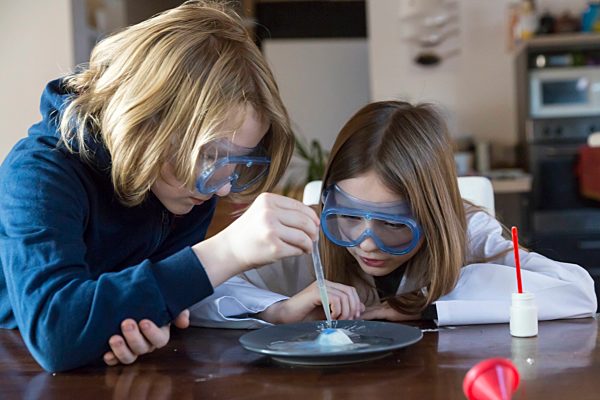 Two children wearing safety glasses using chemistry set at home