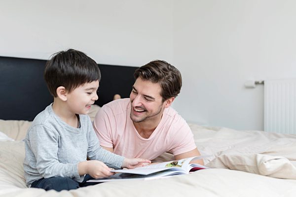 Happy father and son reading a book in bed