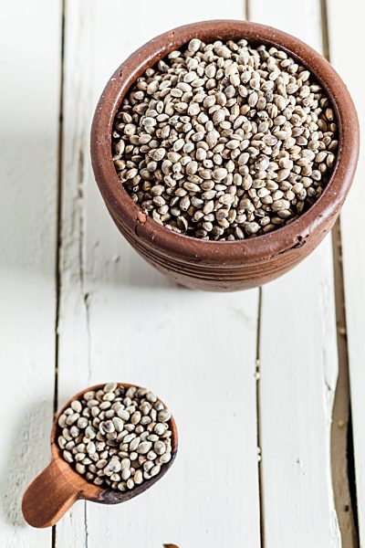 Earthenware dish and wooden spoon of organic hemp seed, Cannabis sativa, on white wood