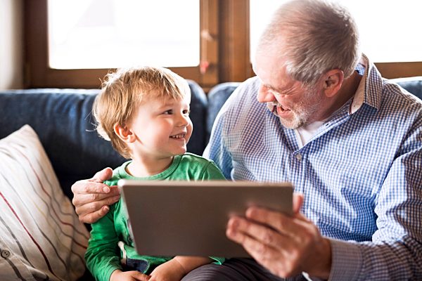Grandfather and grandson sitting on couch, using digital tablet