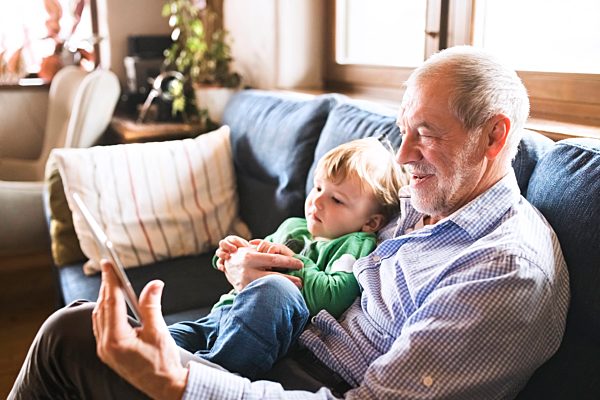 Grandfather and grandson sitting on couch, using digital tablet