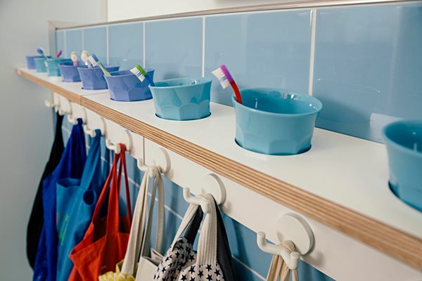 Line-up of of toothbrushes and bags on hooks in kindergarten