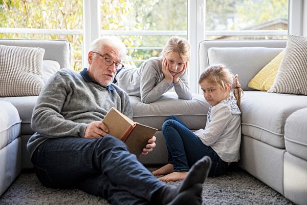 Two girls and grandfather reading book in living room