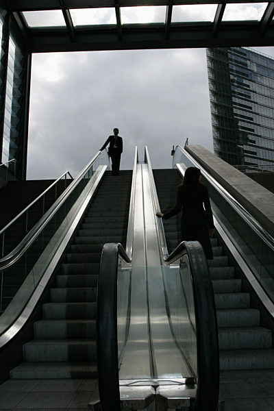 A businessman and a businesswoman riding an escalator