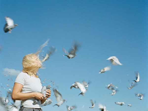 A woman holding a pigeon as other pigeons fly around her