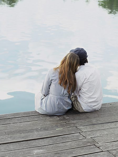 A young couple sitting on a jetty, rear view